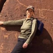 Liesl Dees, UUCB Ministerial Intern, white woman smiling with brown hair, standing with her hand in the crack of a rock that has Native American drawings of animals