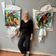 Artist Kim Thoman standing in her Art Studio with art work on either side of her