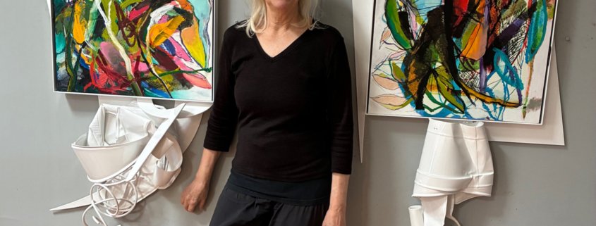 Artist Kim Thoman standing in her Art Studio with art work on either side of her