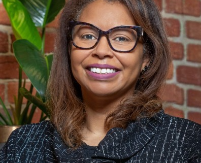 Image of a vibrant African American woman with shoulder length hair wearing glasses and the a navy blue dress.